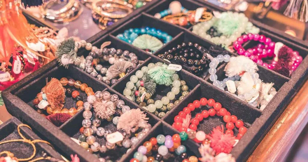 Bandeja organizadora exhibiendo múltiples pulseras artesanales elaboradas con cuentas de colores, piedras y borlas de hilo decorativas.