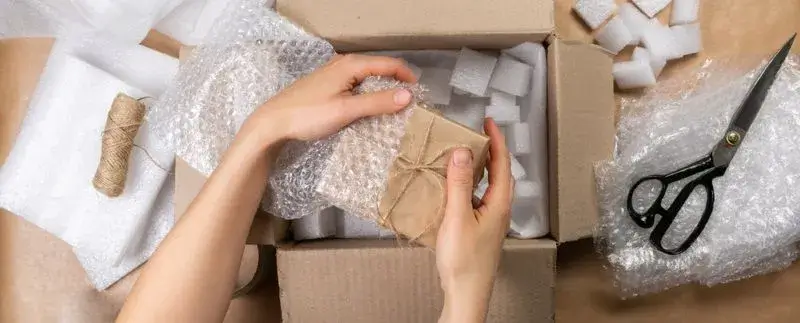 Persona organizando y empacando productos en cajas de cartón desde una mesa en su casa.